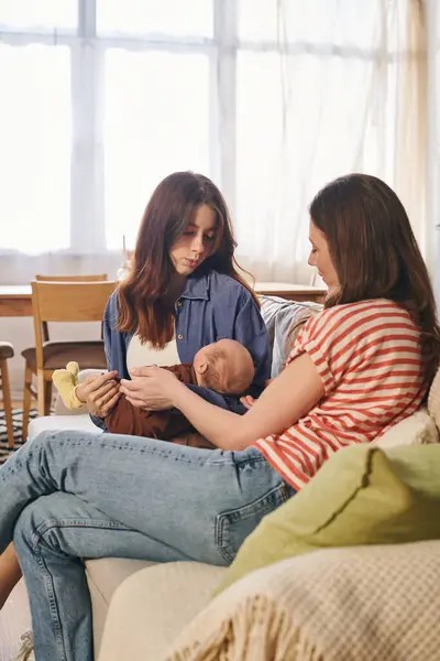 Two mothers tenderly engage with their baby in a cozy home, celebrating their bond. — Stock Photo