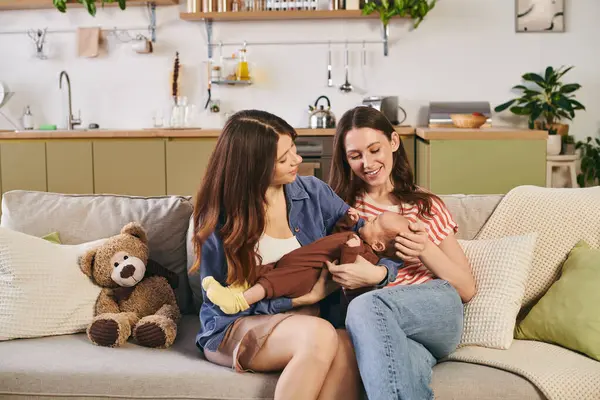 Two loving mothers share a warm Mothers Day moment with their newborn in a cozy home setting. — Stock Photo