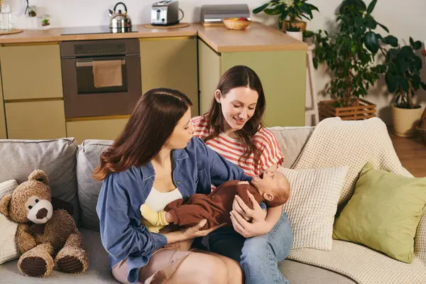 Two loving mothers share a tender moment with their newborn in a cozy home for Mothers Day. — Stock Photo