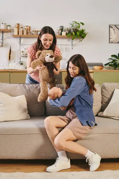 Deux mères aimantes partagent un moment chaleureux avec leur enfant et un ours jouet dans leur salon confortable. — Photo de stock