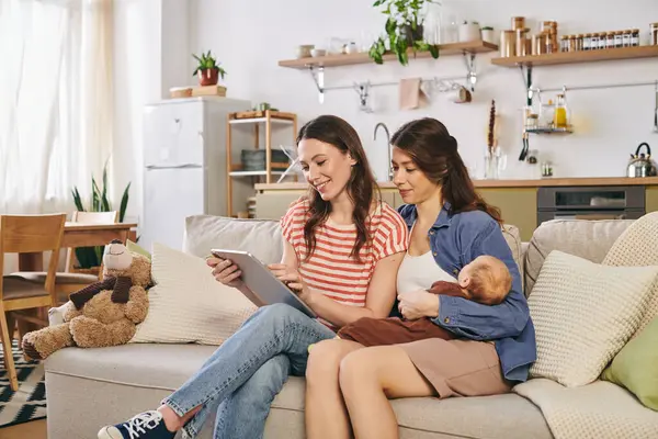 Zwei Mütter genießen einen herzlichen Muttertag in ihrem gemütlichen Zuhause mit ihrem Baby und teilen dabei ihr Lächeln. — Stockfoto