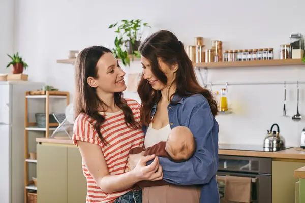 Two loving mothers share a joyful moment with their baby in a warm, inviting kitchen setting. — Stock Photo