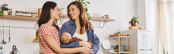Two joyful mothers in a warm kitchen lovingly bond as they celebrate Mothers Day with their baby — Stock Photo