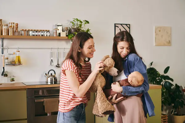 Two joyful mothers lovingly engage with their infant child in a warm, inviting kitchen. — Stock Photo