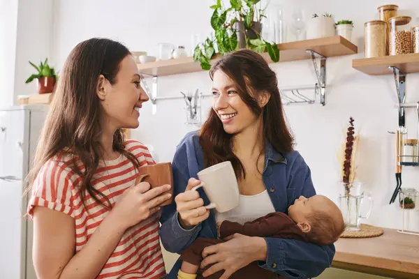 Two joyful mothers enjoy their special day while sharing smiles in a warm kitchen. — Stock Photo