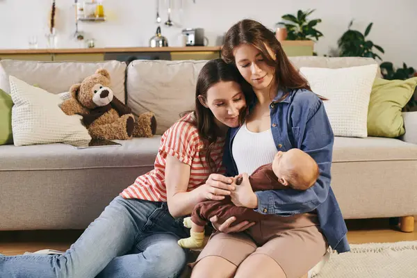 Two loving mothers share a tender moment with their baby in a warm, inviting living room. — Stock Photo