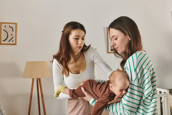 Two loving mothers share a tender moment while caring for their baby in a cozy living space. — Stock Photo