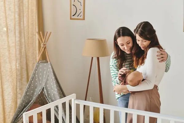 Two loving mothers share tender moments with their baby girl in a warm, inviting nursery. — Stock Photo