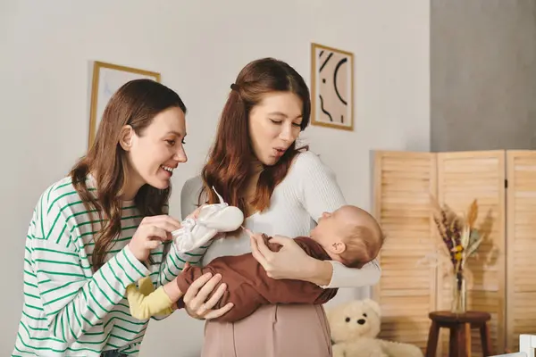 Two loving mothers share a sweet moment with their baby, enjoying Mothers Day in a cozy home. — Stock Photo
