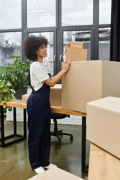 A woman organizes boxes in a modern office while packing for a move, surrounded by plants. — Stock Photo