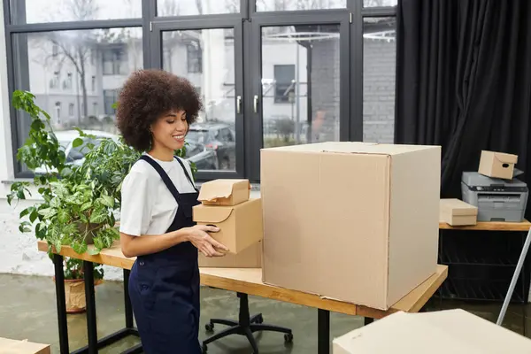 A woman is packing boxes in a sleek workspace surrounded by greenery, preparing for a move. — Stock Photo