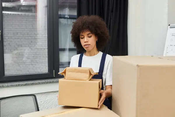 A young adult carefully unpacks a small box in a stylish and modern office environment. — Stock Photo