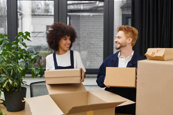 Zwei Menschen sortieren fröhlich Umzugskartons in einem modernen Büro mit nahe gelegenen Pflanzen. — Stockfoto