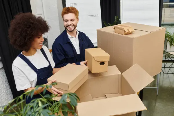 Dois amigos felizmente classificar e lidar com várias caixas em um ambiente de escritório contemporâneo, enquanto se move. — Fotografia de Stock