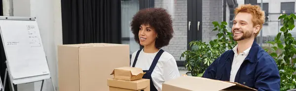 Two individuals, smiling and satisfied, carry packed boxes in a contemporary indoor setting. — Stock Photo