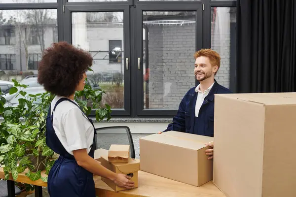 Zwei Personen packen in einem modernen Büro voller Pflanzen Kisten ein und aus. — Stockfoto