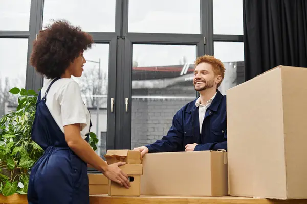 Two friends share a laugh while packing boxes in a bright, green filled room. — Stock Photo