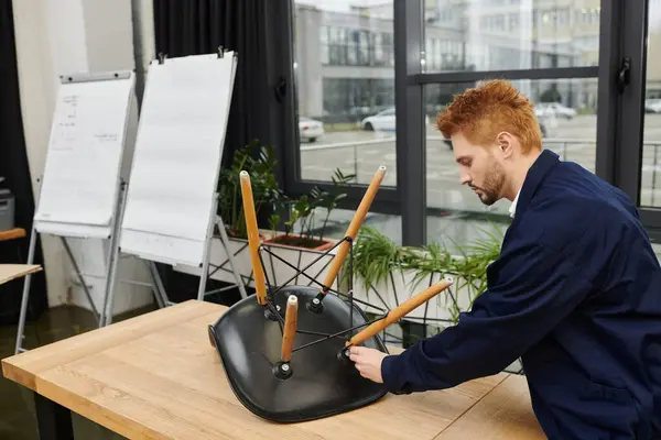 Um homem desmonta metodicamente uma cadeira para se preparar para a realocação em um ambiente de escritório moderno. — Fotografia de Stock