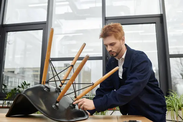 Un joven desmonta cuidadosamente una silla mientras se prepara para un movimiento de espacio de trabajo. - foto de stock
