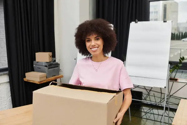 Una donna felice disfa una scatola in un ufficio elegante, godendo il processo in movimento. — Foto stock