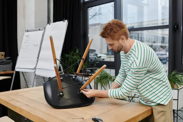 Un joven se centra en armar una silla en un espacio de trabajo moderno mientras se traslada. - foto de stock