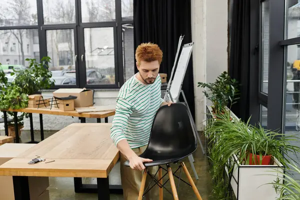 Hombre maneja cuidadosamente una silla negra mientras desempaca en un entorno de oficina contemporáneo. - foto de stock