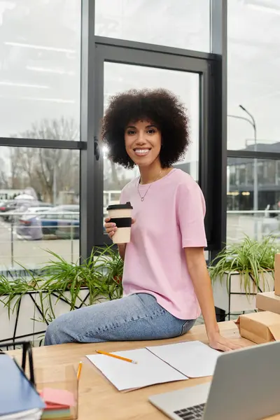 A joyful woman sips coffee at a table, surrounded by packing materials in a modern workspace. — Stock Photo