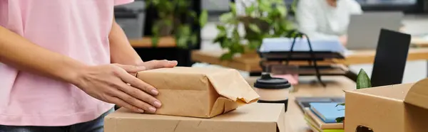 Hands wrap a small package while the workspace buzzes with activity and plants adorn the tables. — Stock Photo