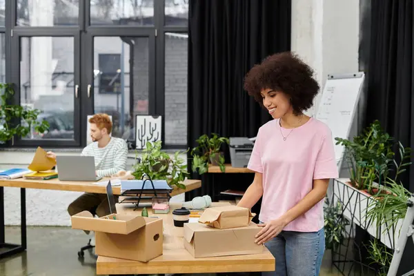 A person unpacks boxes in a bright, plant filled workspace while another concentrates. — Stock Photo