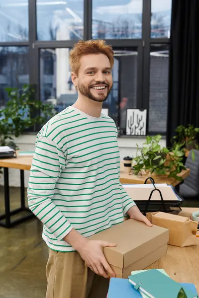 A cheerful man confidently packs a box in a contemporary office space adorned with greenery. — Stock Photo