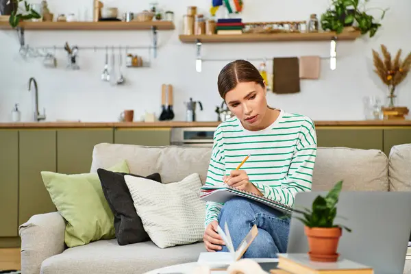 Une jeune femme écrit joyeusement sur une table de cuisine confortable, entourée d'une atmosphère lumineuse. — Photo de stock