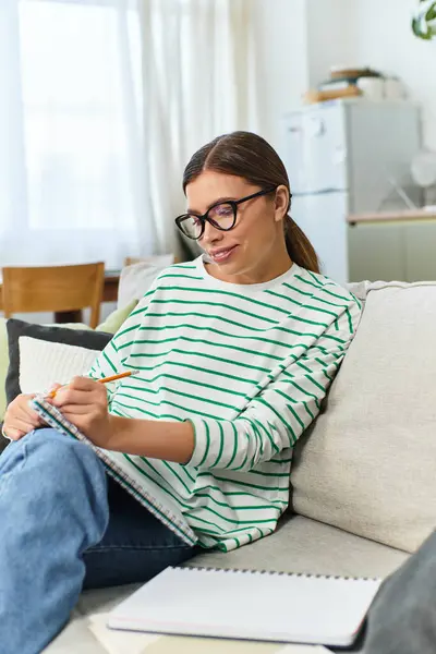 In a cozy living room, a young woman sketches with a pencil while sitting comfortably. — Stock Photo