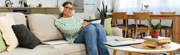 A young woman relaxes on a sofa, writing and listening to soothing music. — Stock Photo
