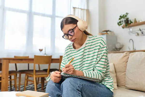 A focused young woman sketches in a modern living area while listening to music. — Stock Photo