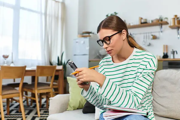 Bright apartment where a young woman is focused on her phone and taking notes. — Stock Photo