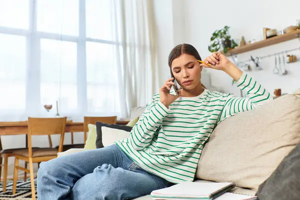 A young woman chats joyfully on her phone while relaxing on a couch in a bright living area. — Stock Photo