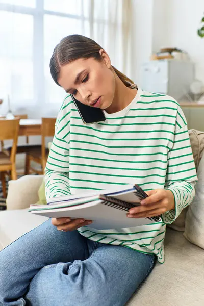 Une jeune femme s'assoit sur un canapé confortable, parle au téléphone et prend des notes dans son carnet.. — Photo de stock