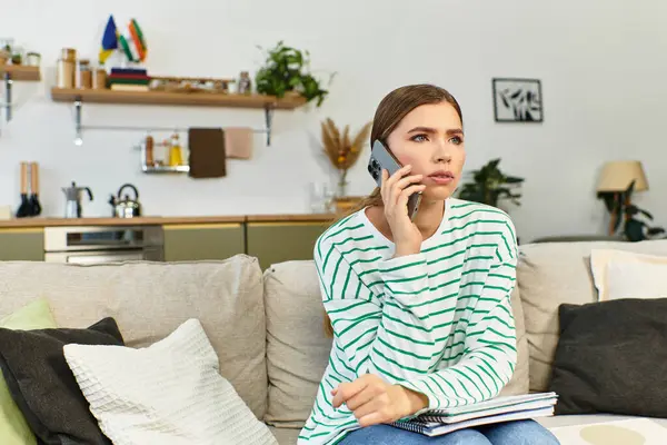 Une jeune femme bavarde sur son téléphone, confortablement assise avec des cahiers à la main. — Photo de stock