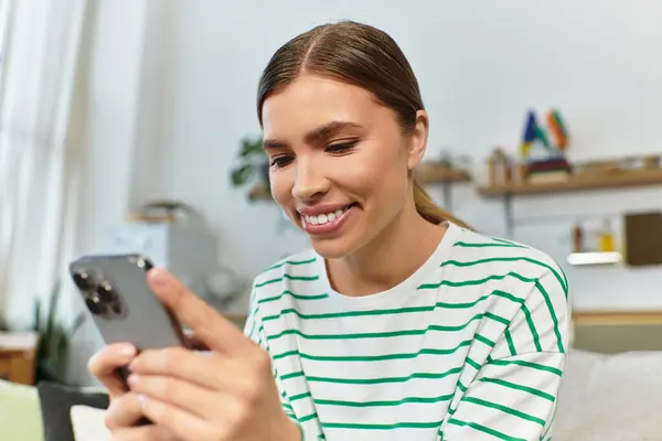 Happy young woman enjoys her smartphone while relaxing on a cozy couch in a chic room. — Stock Photo