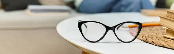 Elegantes gafas de ojo de gato yacen en una mesa de café elegante, mujer en el sofá. - foto de stock