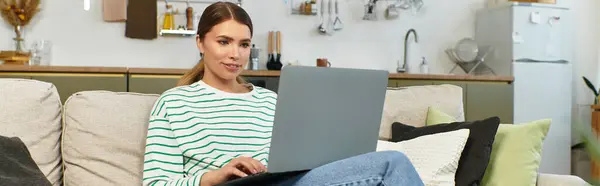 Una giovane donna si rilassa su un divano, concentrata sul suo computer portatile in un tranquillo pomeriggio. — Foto stock