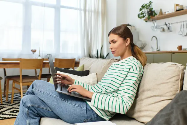 In a bright living space, a young woman relaxes on the sofa, focused on her laptop. — Stock Photo