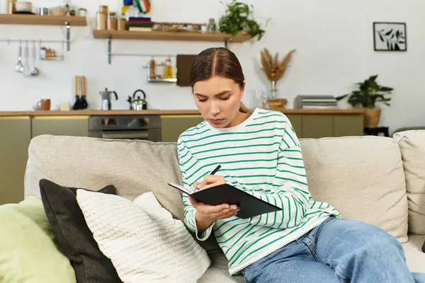 A young woman relaxes on a cozy couch, jotting notes amid modern decor. — Stock Photo