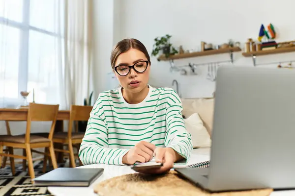 A beautiful woman with glasses focuses on her work at a stylish table surrounded by plants. — Stock Photo