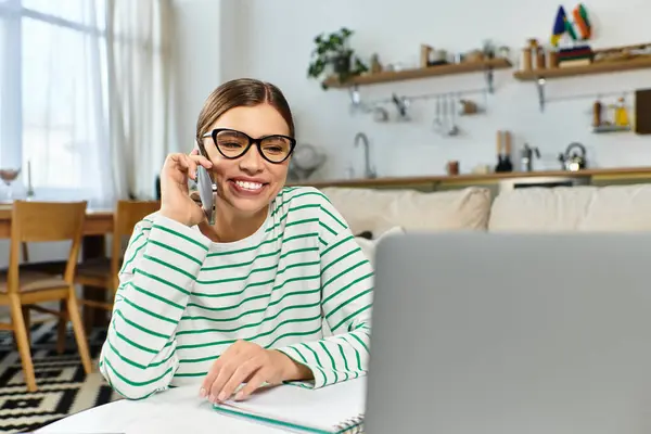 Une jeune femme souriante engage une conversation téléphonique dans son élégant bureau à domicile pendant la journée. — Photo de stock