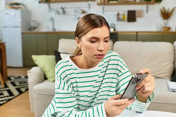 Brightly lit living room features a young woman in striped attire focused on her smartphone. — Stock Photo