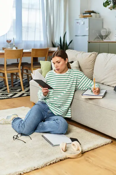 Une jeune femme lit et prend des notes sur le sol d'un salon lumineux et minimaliste. — Photo de stock