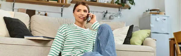 Inside a stylish apartment, a young beautiful woman talks on the phone while relaxing on the couch. — Stock Photo
