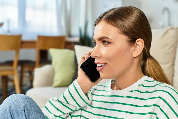 La sala de estar luminosa cuenta con una mujer joven que participa en una llamada telefónica animada mientras se relaja. - foto de stock