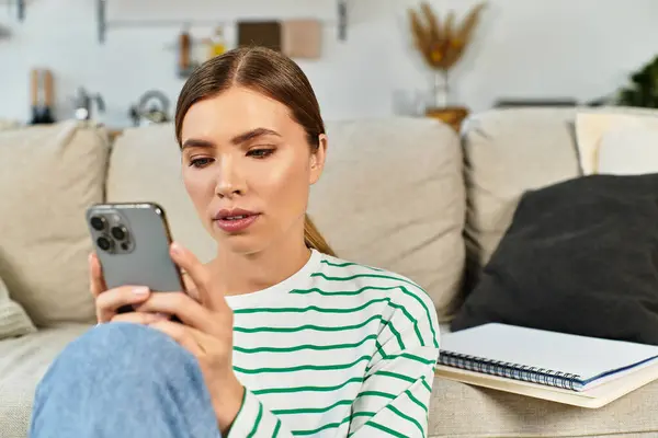 Femme utilise attentivement son smartphone sur un canapé confortable dans un cadre élégant de la maison. — Photo de stock